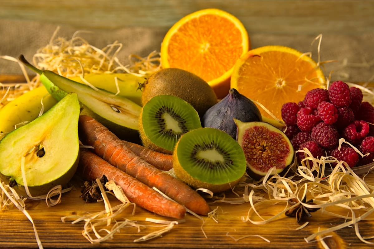 Étalage de fruits coupés sur une planche : poire, kiwi, figue, orange, framboises, banane et carottes