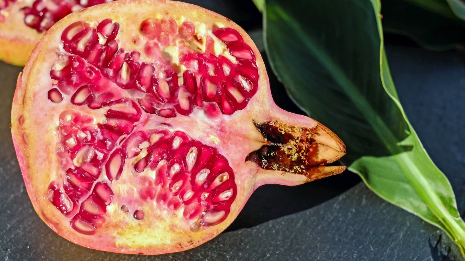 Grenade coupée en deux : des centaines de grains rouges serrés dans leurs loges, dont plusieurs laissent voir par transparence la graine pâle qu’ils contiennent. (Photo couleur, Pixabay.)