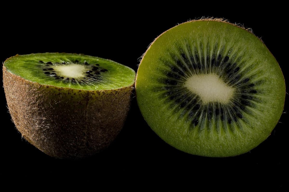 Kiwi coupé en deux sur fond noir : les rayons blancs partant du cœur pâle, et les graines noires alignées entre eux